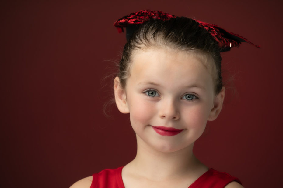 Studio portrait by Schoolhouse Photos: a young dancer in red smiling against a deep red backdrop