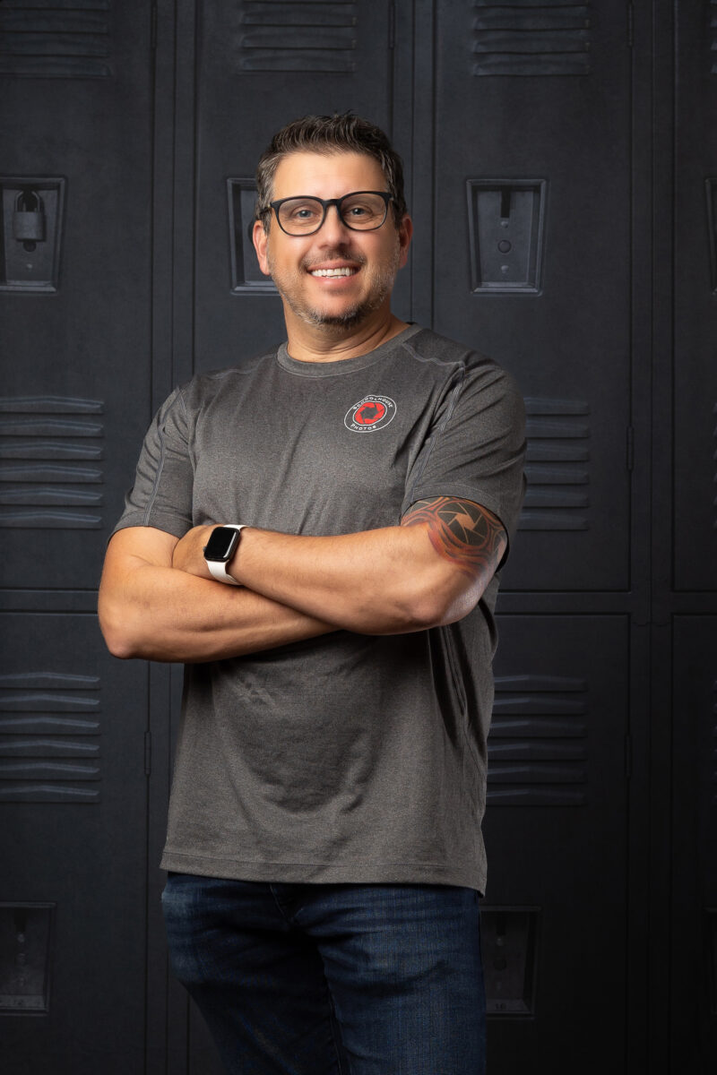 Michael Snyder, founder of Schoolhouse Photos, smiling with arms crossed in front of a wall of school lockers
